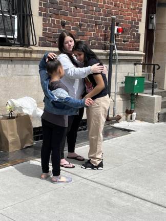 A teacher at the Guardian Angel School leans in to embrace two tearful students of hers. Since the school is closing for good, they will not return.