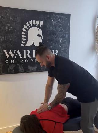 Dr. Johnny Alexander and a patient at Warrior Chiropractic. Note the vertebrae on the Roman Centurion helmet logo in place of the classic feathers.