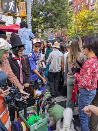 The crowd at East 10th and Avenue B, Beastie Boy and dog in New York sports gear and chain crossing the street.