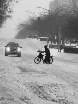 Another delivery worker crosses the street as snow falls heavily on Park Ave. on the Upper East Side