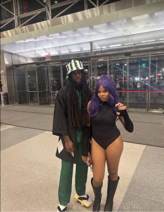 A pair of cosplayers portray Kisuke Urahara in signature green-and-black attire with striped bucket hat and wooden sandals alongside Yoruichi Shihoin in a black bodysuit near the exit.
