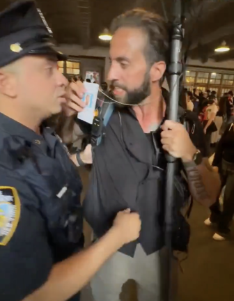 Man with camera on stick shows cop his press pass.