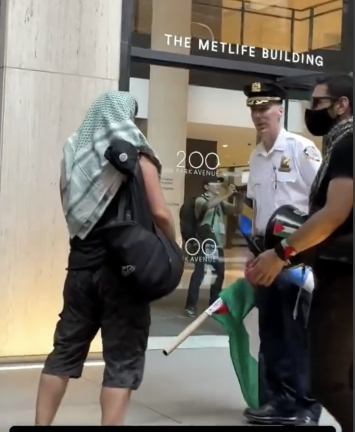 Keffiyeh man in conversation with Deputy Inspector Timony Beaudette outside the MetLife Building, as a masked Palestinian drummer looks on.