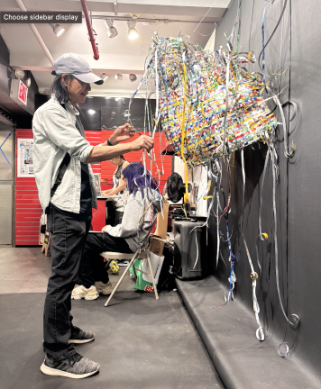 Artist Chin-Chih Yang adjusts a sculpture made from cut aluminum cans while installing <i>23 Pollution Solution</i> at Whitebox Portable.