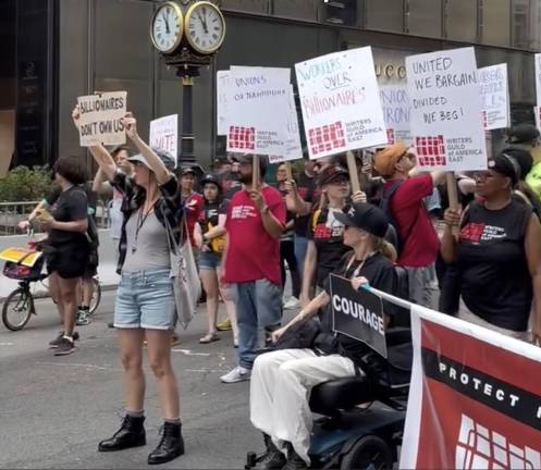 “Billionaires Don’t Own Us” and other signs held by Writers Guild of America East marchers.