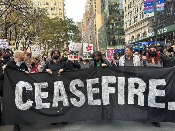 People holding a sign demanding a ceasefire.