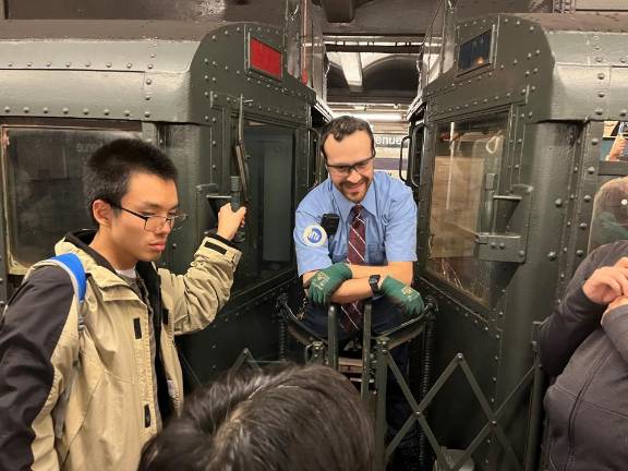 Giving an impromptu Q&amp;A to delighted passengers, a well-dressed Transit Authority conductor speaks to them between the cars. With the museum equipment, there are always lots of questions.