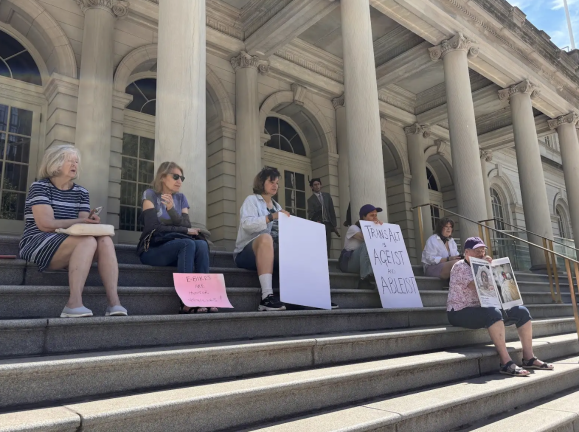 Participants gather in the shade outside City Hall before a June 25 news conference announcing a lawsuit challenging Mayor Zohran Mamdani’s e-bike enforcement policy.