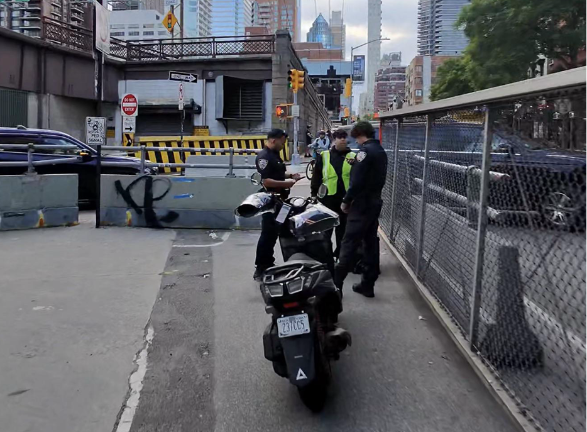 Police write out a summons on the afternoon of May 29 to a person who was driving a motorized vehicle that is banned from the bike lane on the Queensboro Bridge. A scooter and a bike collided in the bike lane the previous day, killing both individuals.