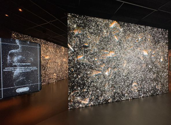 The final space in the exhibition is “The New Beginnings Hall.” Visitors can draw on the screen depicted on the left, and then see their creation float across the larger starry screen on the right.