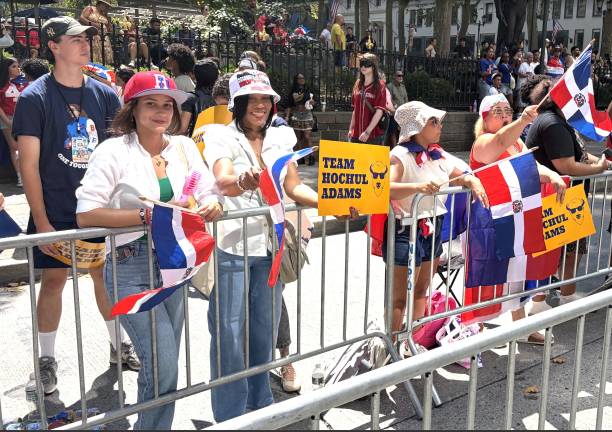Domincan Day Parade dazzles mega multitudes in Midtown, here with people holding out Team Hochul Adams signs in symbolic opposition to DSA.