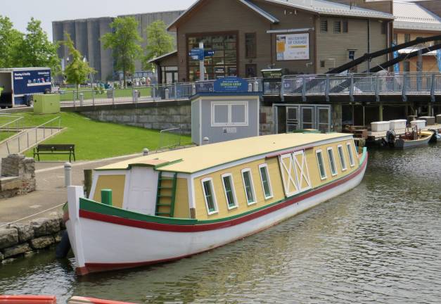 With the “Waterway of Change” exhibit in the background and the <i>Seneca Chief i</i>n the foreground, the 200th anniversary of the Erie Canal opening is a big event in the Canalside part of Buffalo. While the “Waterway of Change” exhibit’s visual displays are informative and deal with social change that the Canal caused, the <i>Chief</i> has a different mission: Starting on Sept. 25, the replica of DeWitt Clinton’s first boat to traverse the Erie Canal will be traveling to NYC for a month, stopping at ports along the existing canal route.