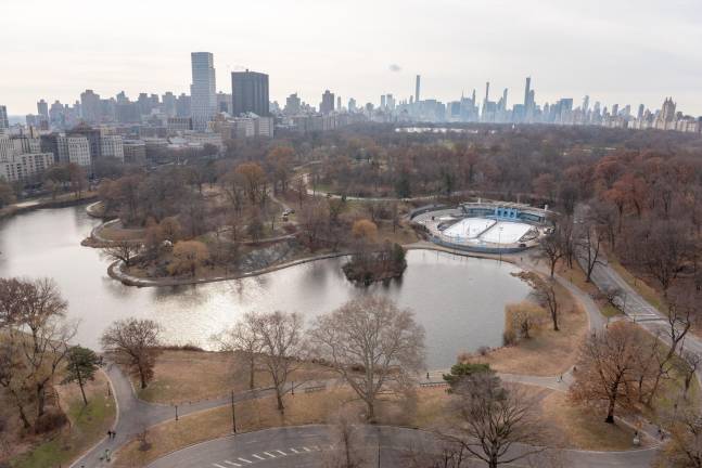 A wintertime photo of the Harlem Meer in Central Park, looking south and east, with the twin ovals that comprise the existing Lasker skating rink and a view of the Manhattan skyline in the background.