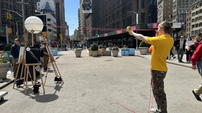 Jack Cruse, from the MoMath Institute of Math showing New Yorkers how the moon (small yellow/green ball he is holding) will go in front of the sun (large white ball sitting on wooden stand) on April 8. Photo Credit: Alessia Girardin.